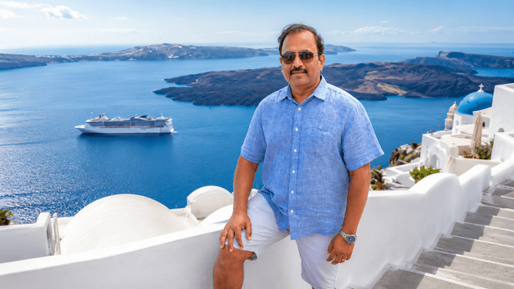 Dr. Vijay Kumar overlooking Santorini's iconic whitewashed buildings, blue-domed churches, and the Aegean Sea from the volcanic cliffs